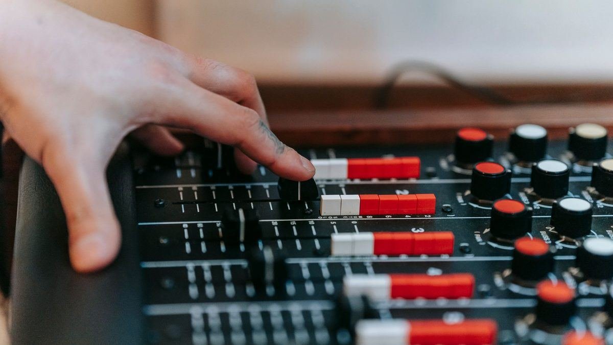 A hand adjusting faders on an audio mixing console